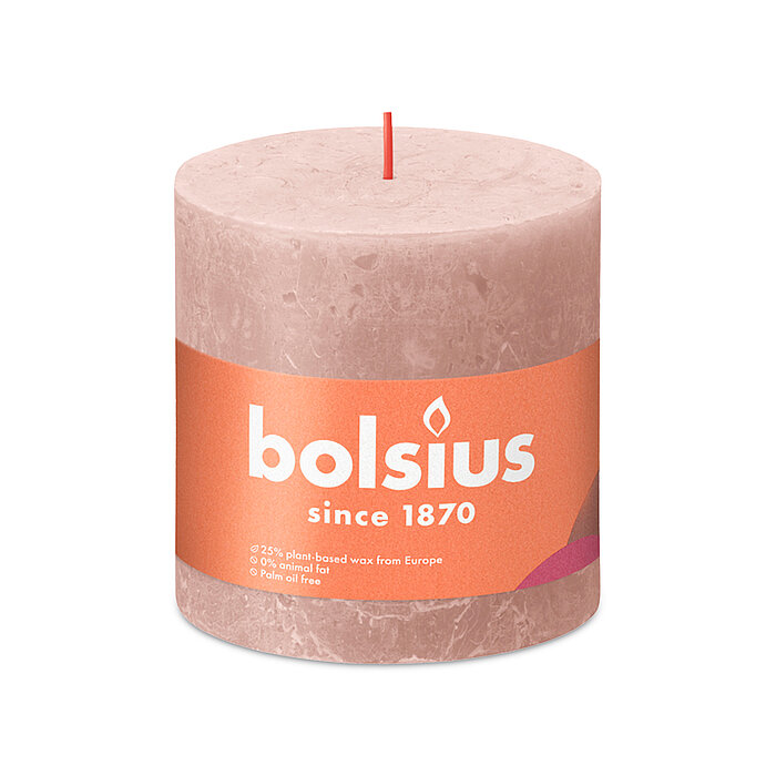 Eine durchgefärbte Rustik Stumpenkerze in der Farbe Nebliges Rosa mit den Maßen 100/100mm (H/DM). Der Banderole kann man die Marke "Bolsius" sowie die Hinweise "25% pflanzenbasiertes EU-Wachs", "0% tierisches Fett" und "Ohne Palmöl" ablesen.