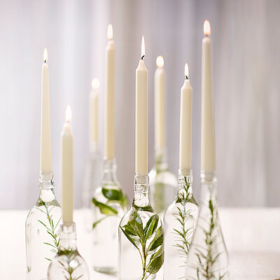 Stilvoll und natürlich dekoriert: Bolsius Professional Tafelkerzen und Spitzkerzen in Glasflaschen mit frischem Grün sorgen für eine elegante, ruhige Atmosphäre bei besonderen Anlässen oder im Alltag.