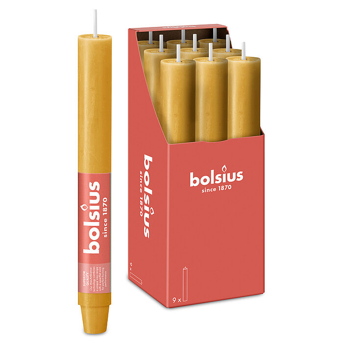 Eine durchgefärbte XL Rustik Haushaltskerze mit konischem Fuß in der Farbe Haferbeige. Im Hintergrund ist ein 9er Pack der Stabkerzen in einer Schachtel von Bolsius zu sehen.