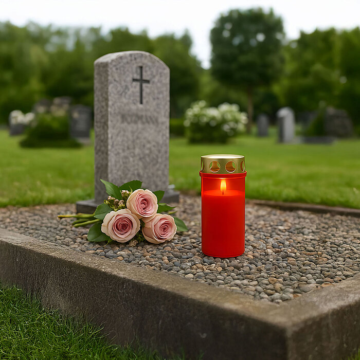 Sanft flackernde Grabkerze mit Deckel – eine rote, wind- und wetterfeste Gedenkkerze mit praktischer Metall-Abdeckung, platziert auf einem gepflegten Grab.