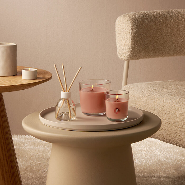 Brennende Duftkerzen in verschiedenen Größen mit rosa Wachs stehen auf einem gemütlichen Wohnzimmertisch neben einem Raumduft Diffuser.
