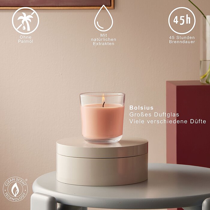 Ein brennendes Duftglas von Bolsius auf einer dekorativen Schachtel in einem modernen Wohnzimmer. Auf dem Bild werden verschiedene Vorteile des Duftglases hervorgehoben und die Brenndauer von 45h dargestellt.